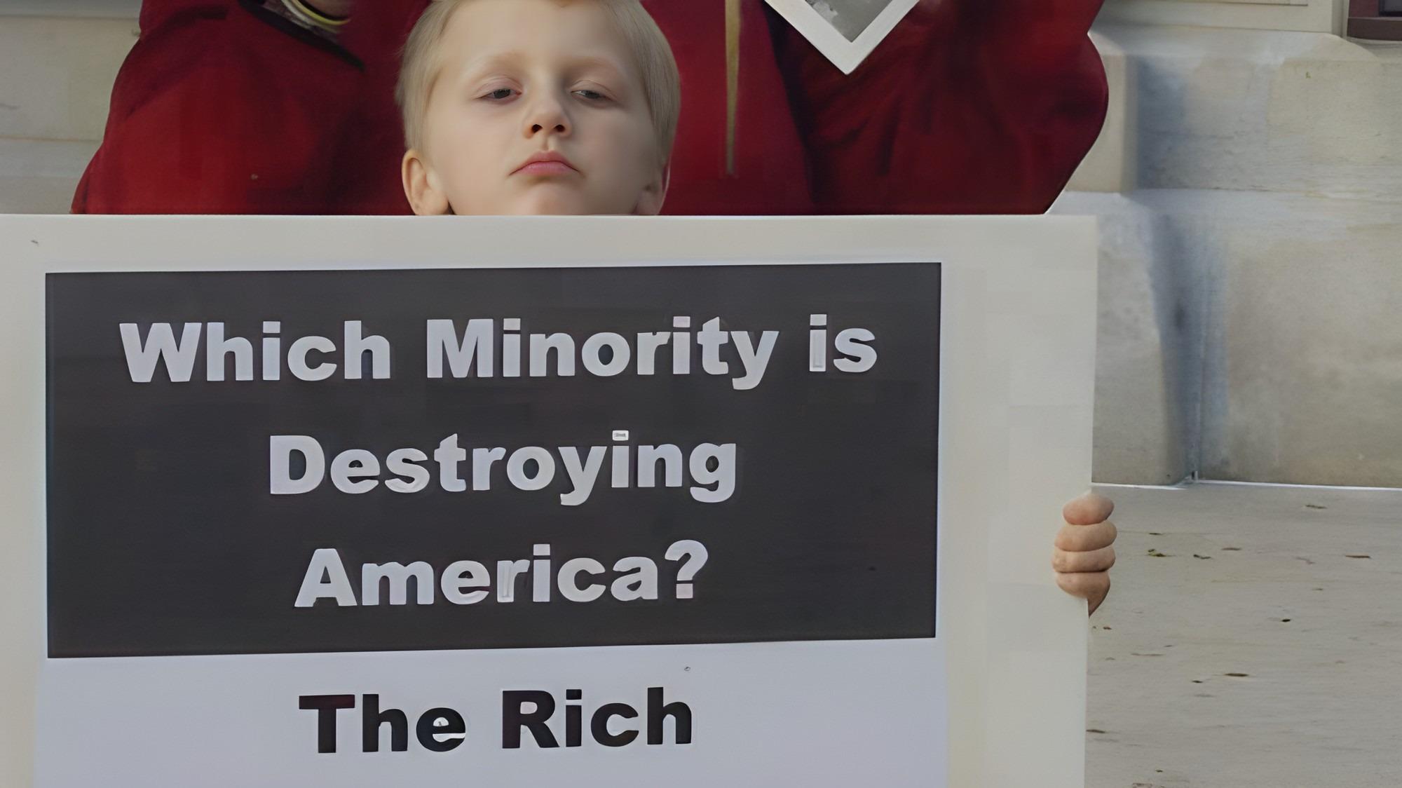A photo of a little boy holding a sign that says, "Which minority is destroying America? The rich." A photo of a little boy holding a sign that says, "Which minority is destroying America? The rich."