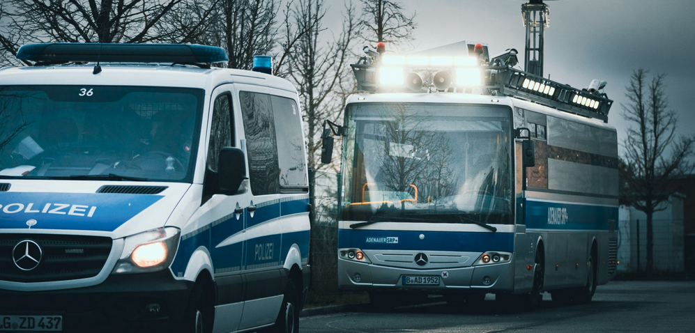 links ein blau-weißer Polizei-VW-Bus. Dahinter ein großer Bus, des Zentrums für politische Schönheit. Die Aufmachung ähnelt einem Justizbus: weiße Farbe, blauer Streifen rund um den Bus. Auf dem Dach des großen Bus sind starke Scheinwerfer und Lautsprecherboxen montiert. links ein blau-weißer Polizei-VW-Bus. Dahinter ein großer Bus, des Zentrums für politische Schönheit. Die Aufmachung ähnelt einem Justizbus: weiße Farbe, blauer Streifen rund um den Bus. Auf dem Dach des großen Bus sind starke Scheinwerfer und Lautsprecherboxen montiert.